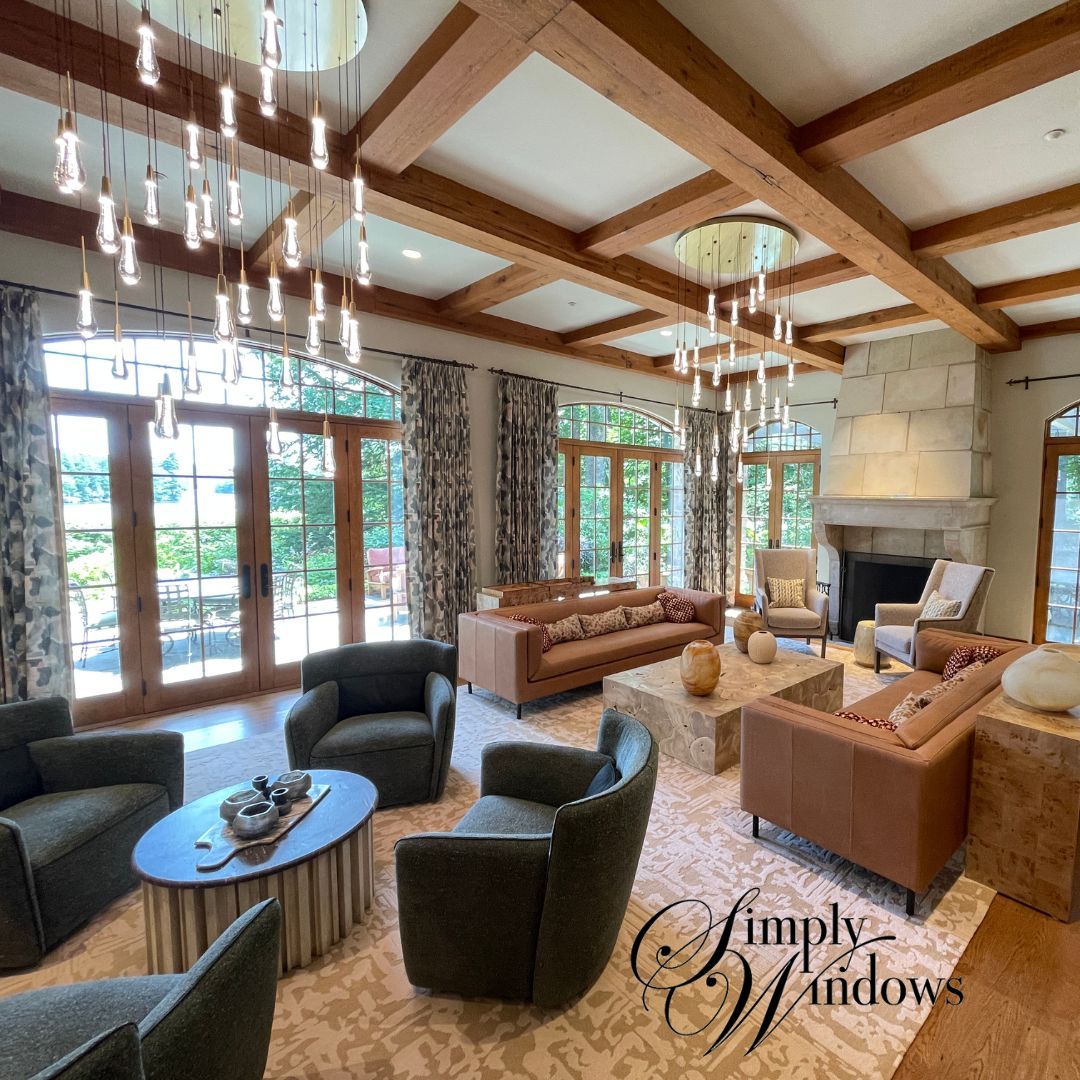 Elegant living room with wood beams, patio doors, modern chairs, sofa, and stone fireplace