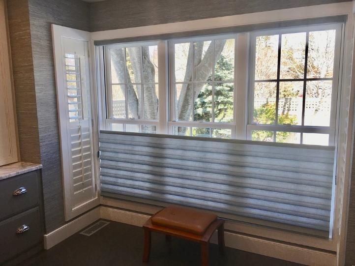 Bathroom window with partially lowered pleated blinds, shutters, and a small brown stool.