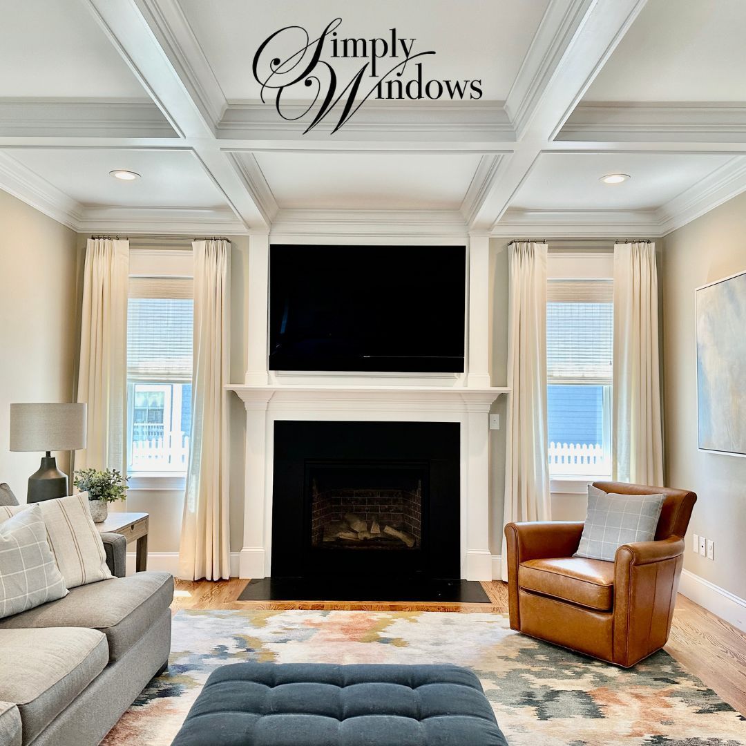 Elegant living room with white coffered ceiling, honeycomb shades, gray sofa, brown armchair, and blue ottoman