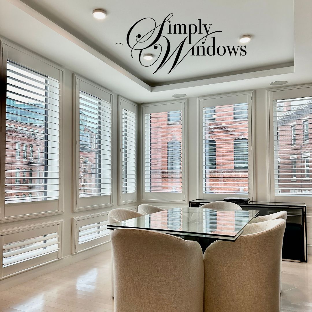 Bright dining room with white plantation shutters and a glass table by large windows