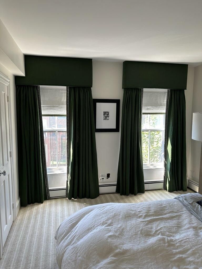 Deep green drapes with cornices decorate the windows in a bedroom. 