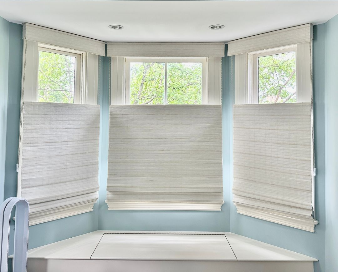 Bright bay window nook with white top-down bottom-up shades and a built-in cushioned bench.