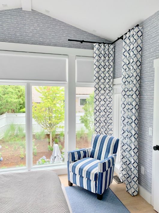 A bedroom has decorative rods for the corner windows holds blue patterned drapes. 