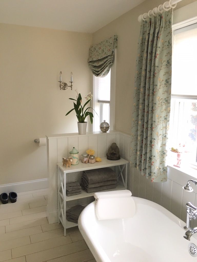 Bathroom with white bathtub, shelves, and floral curtains.