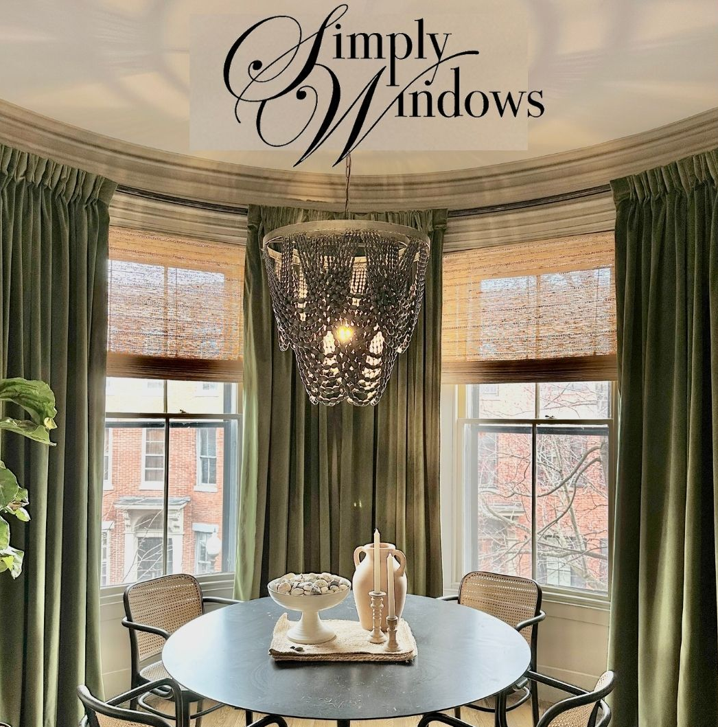 Dining room with custom green drapes, chandelier, round table, and city view through windows.