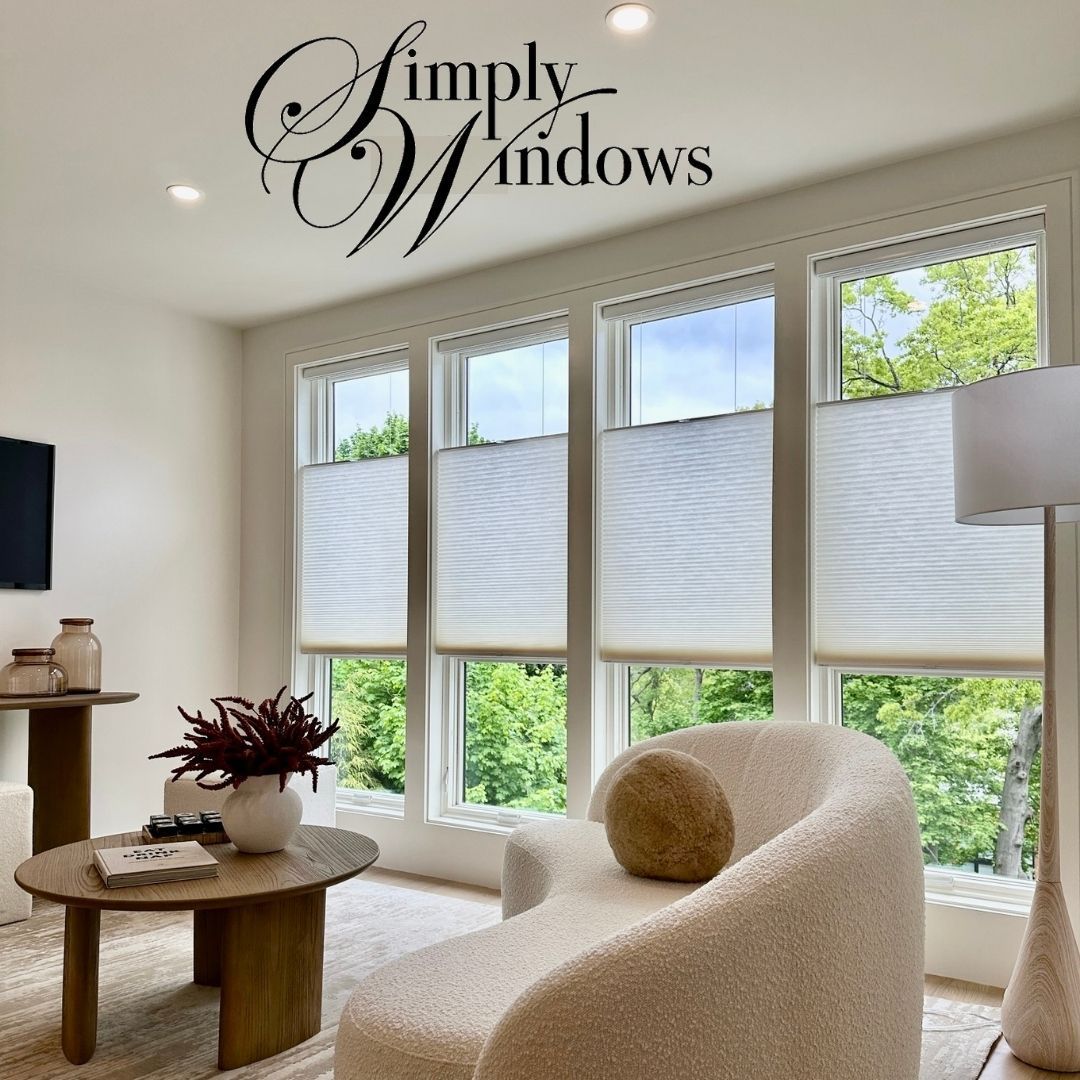 A modern, sunlit living area features four floor-to-ceiling windows with top-down cellular shades, a sofa, and coffee table.