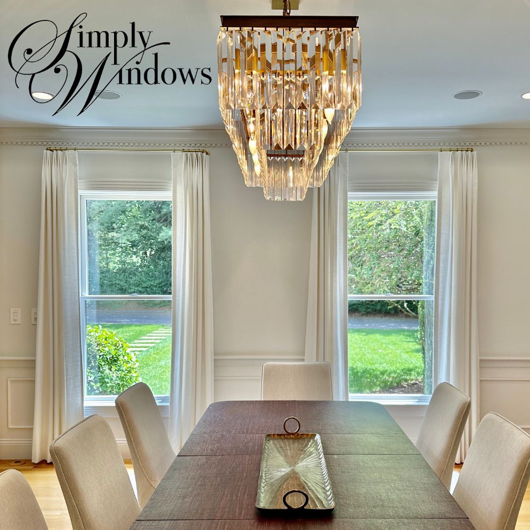 Dining room with two windows, chandelier, table, chairs, and white curtains.
