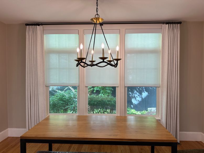 An elegant chandelier is lit above a dining table, and custom window treatments are in the background. 