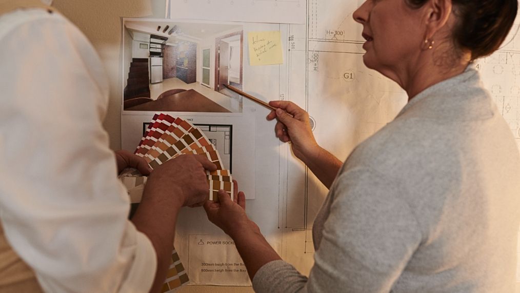 two women are looking at a blueprint  of a room and swatches Simply Windows.