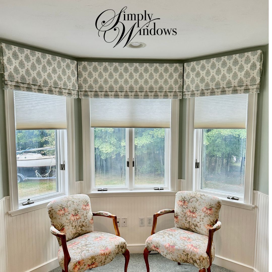 An elegant sitting nook with a bay window has roman shades and solar shades layered - simply windows