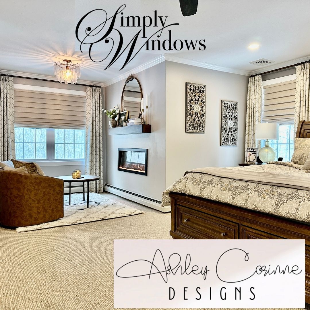 A bedroom with a bed, seating area, fireplace, and windows covered with patterned shades and curtains.