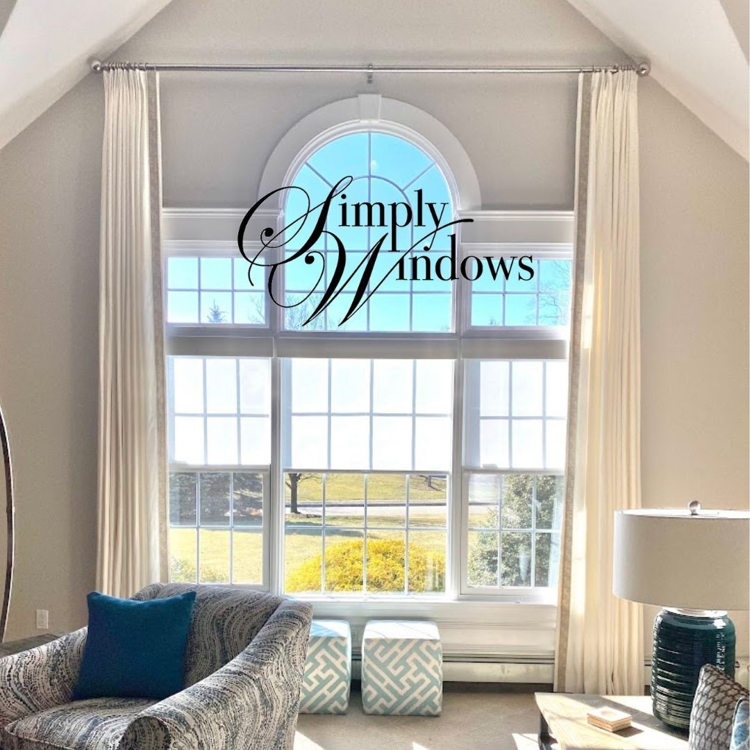 Living room with large arched window, white curtains, and furniture. Logo overlay reads 