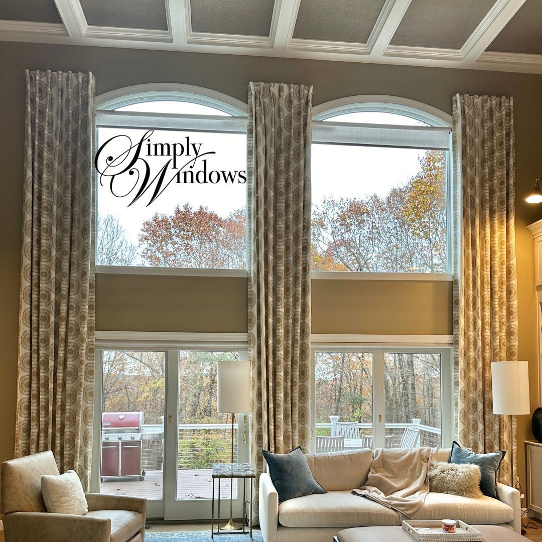 Tall patterned floor-to-ceiling curtains frame arched windows above a living room with a couch and armchairs.