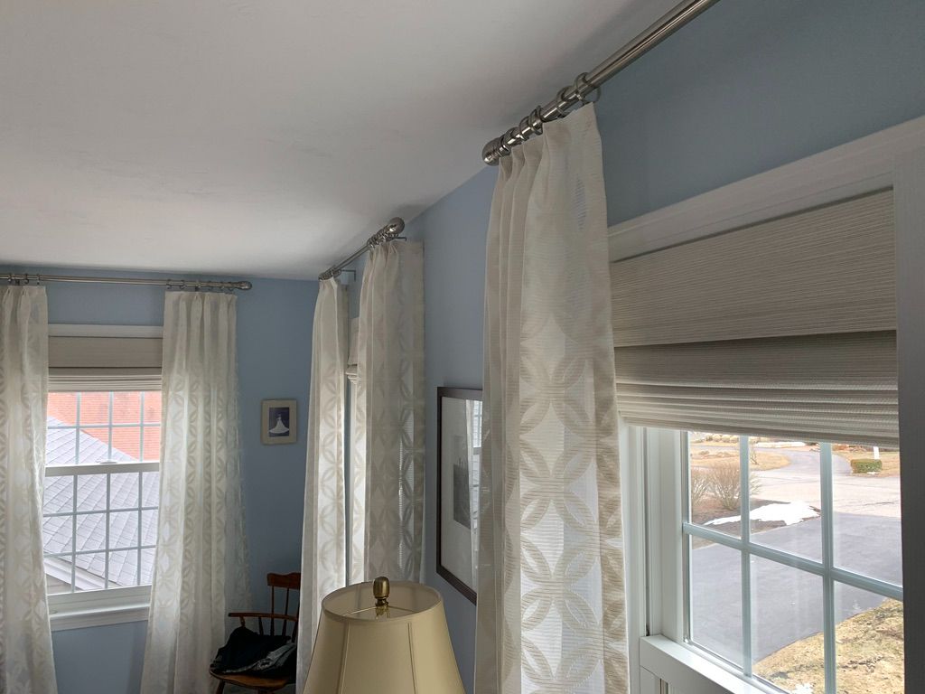 A close up view of custom silver curtain rods, drapes, and roman shades in a blue room. 