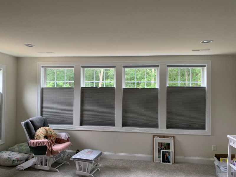 A gray room has 4 windows with roller shades to naturally filter light. 