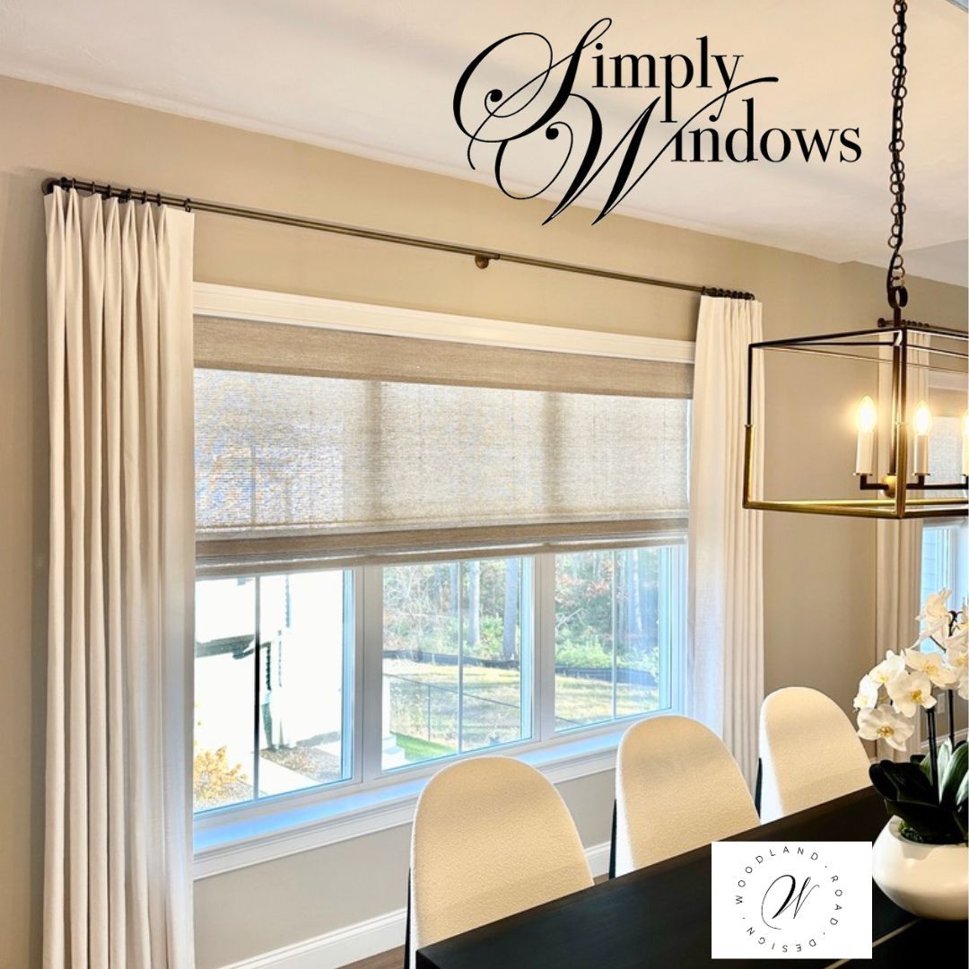 Dining room window with beige woven shades, off-white curtains on a dark rod, and a modern chandelier overhead.