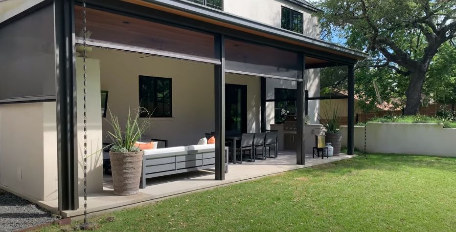 A house with a covered porch, motorized exterior shades, and a lawn in front of it.