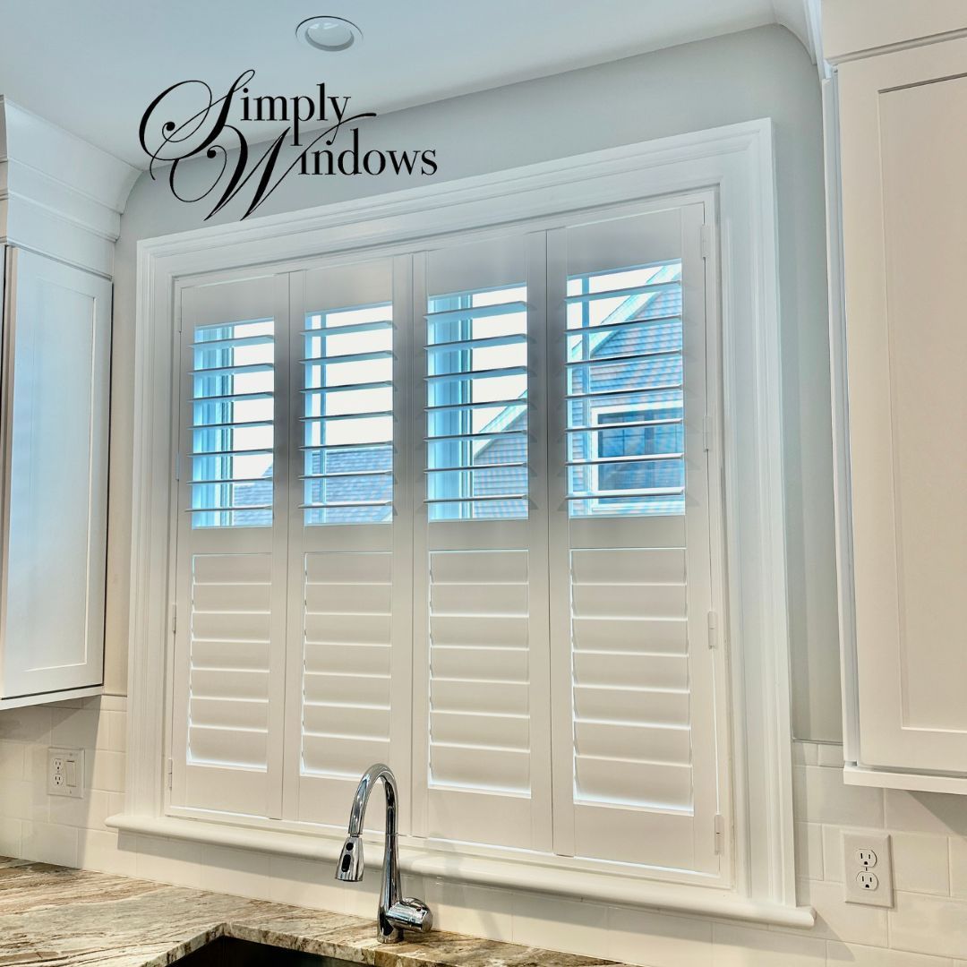White plantation shutters installed on a kitchen window above a sink, with a Simply Windows logo in the corner.