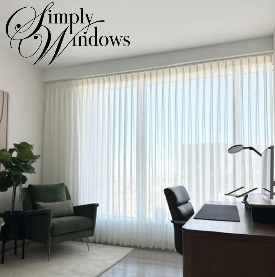 Office with white sheer curtains, green armchair, and desk by a large window.