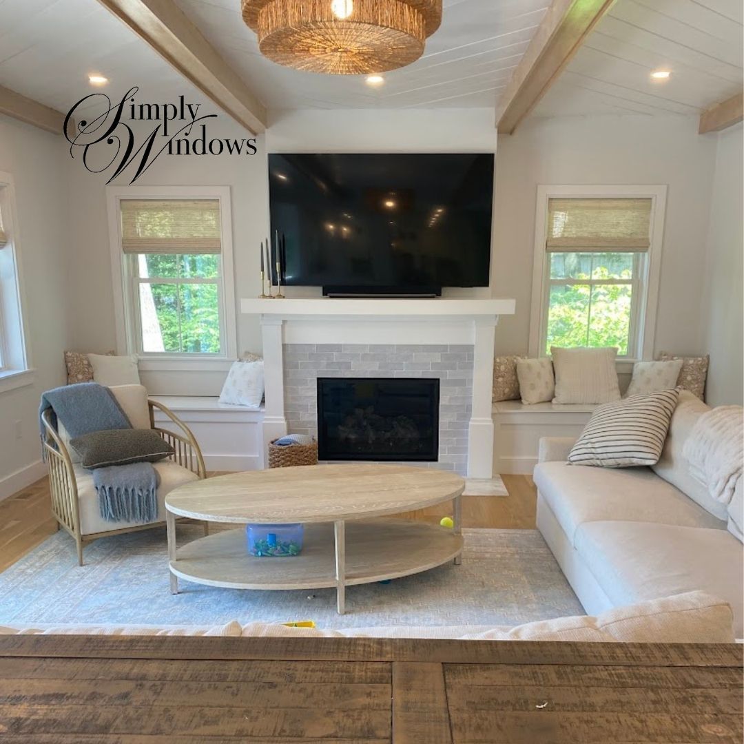 A bright, coastal-style living room with a white fireplace, large TV, cozy seating, and built-in window benches.