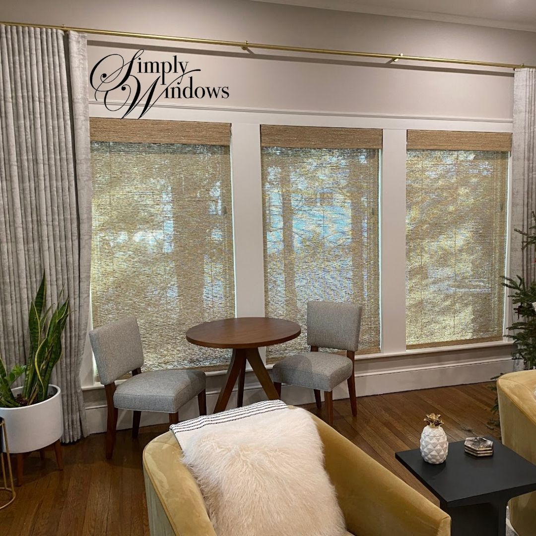 Living room with three windows featuring light brown woven shades, a small round table, and armchairs.