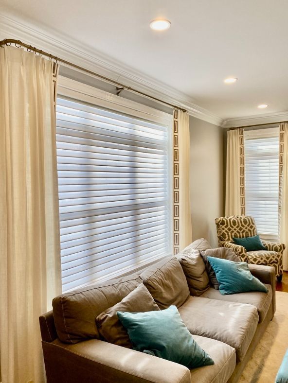 Tan drapes frame a living room window with white cellular shades, a couch is in front. 