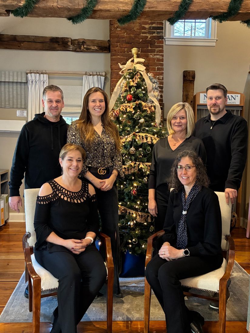Group of seven people posing in front of a Christmas tree in a room with exposed beams.