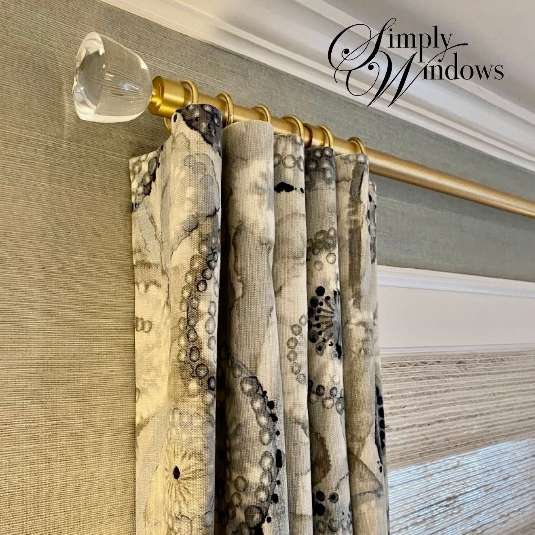 Curtains with a gray, abstract, circular pattern hanging from a gold rod with a clear crystal finial.