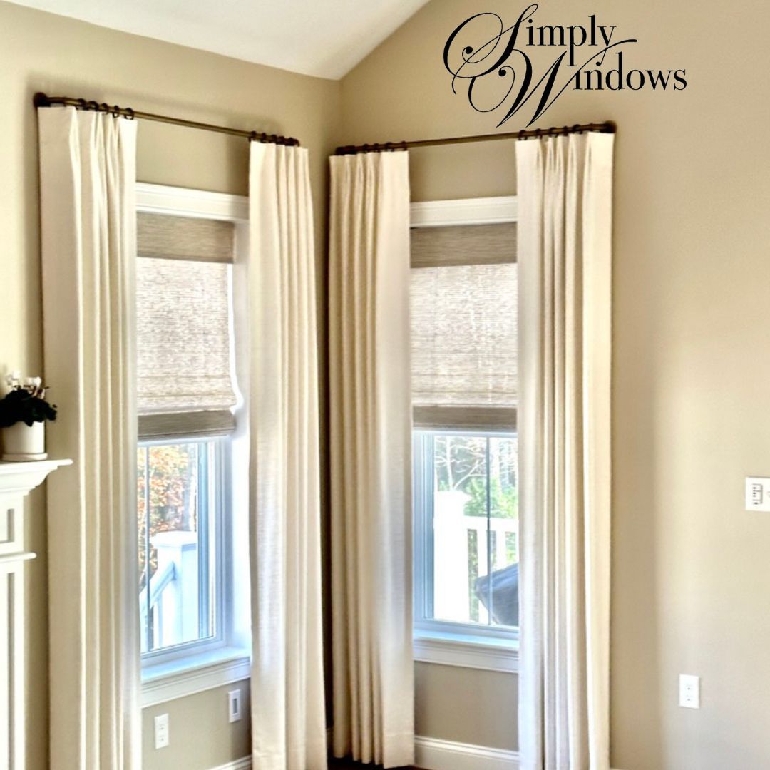 Cream curtains framing two tall windows with woven wood shades. 