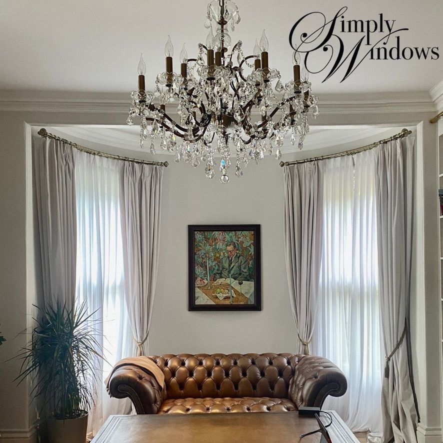 Elegant living room with a crystal chandelier, tufted sofa, sheer curtains, and framed artwork