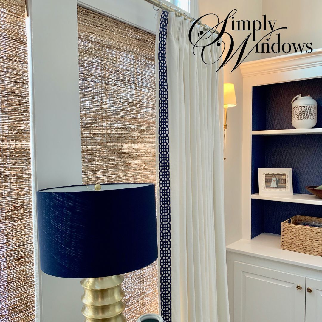 Window with woven shades and custom drapery beside blue lamp and built-in shelving in a bright room
