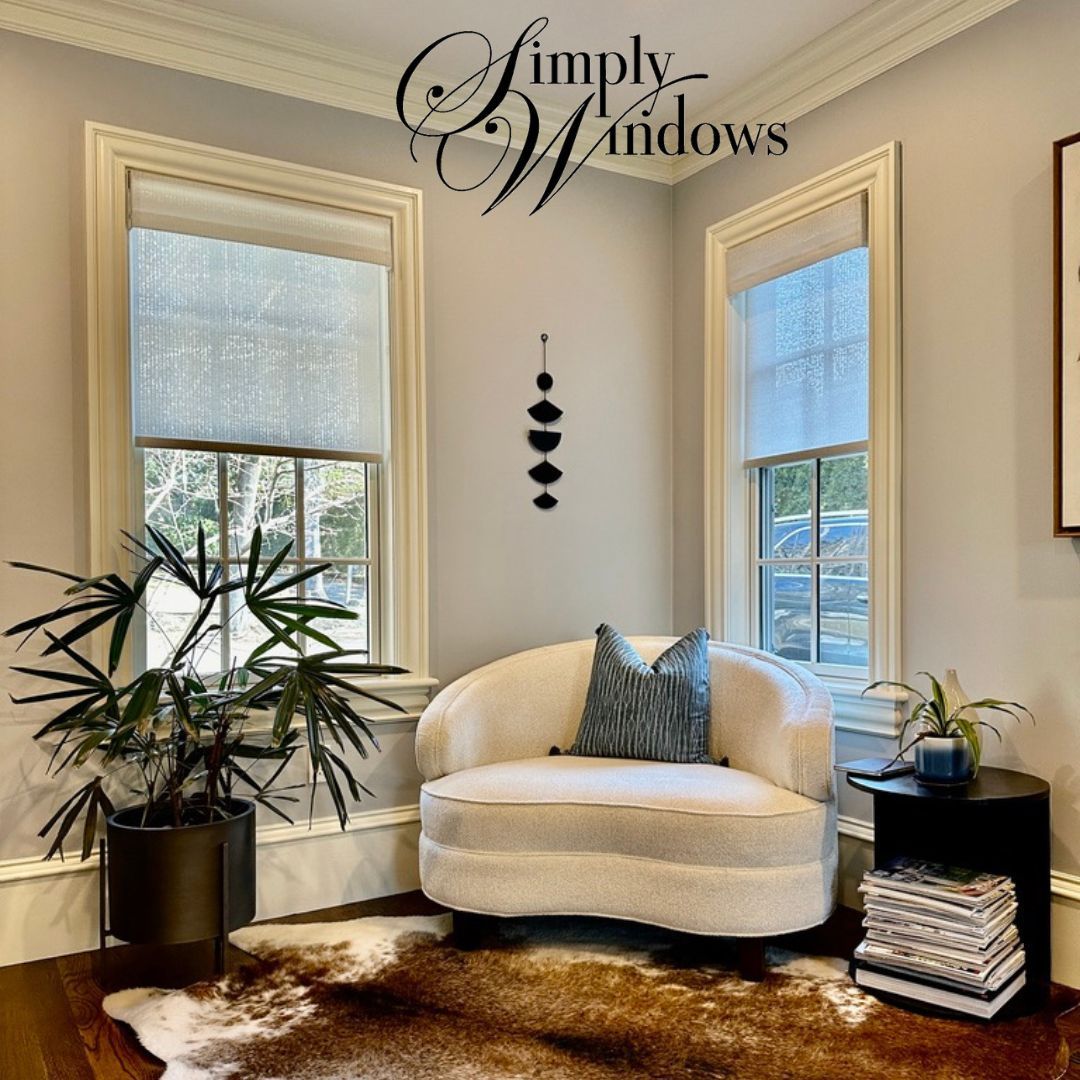 A beige chair sits in an elegant, yet cozy corner with windows covered with roller shades - simply windows, ma