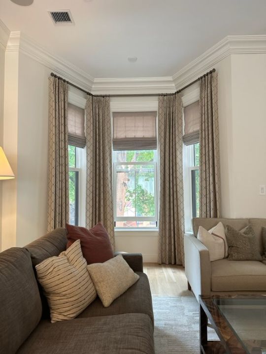 Simply Windows: A living room with a couch and two windows with custom drapery and Roman shades.