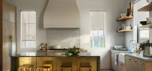 Modern kitchen with brass island, white cabinets, and large white range hood.