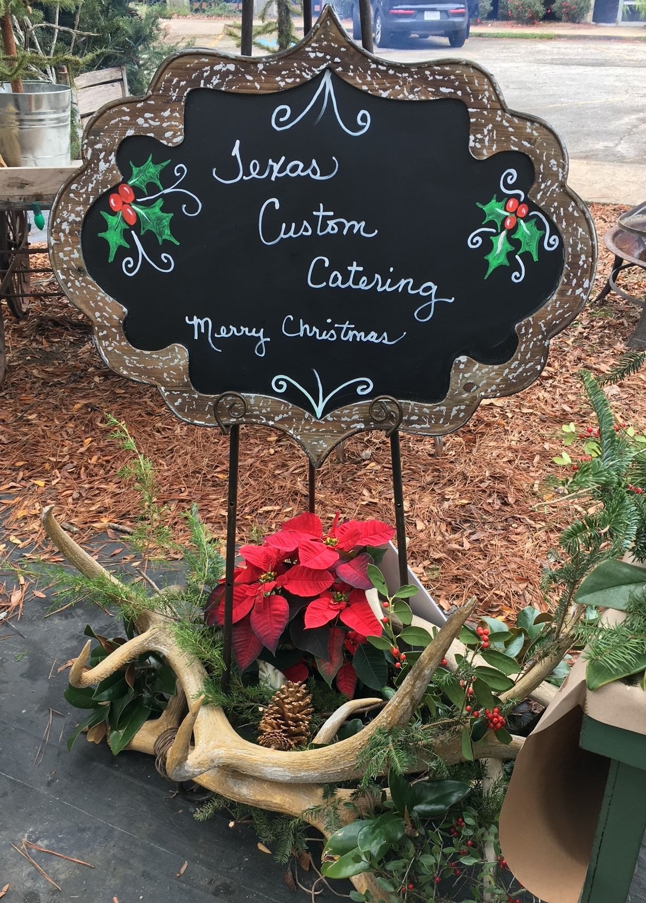 Chalkboard sign for Sienna's Custom Catering above poinsettias and decorative wreaths outdoors