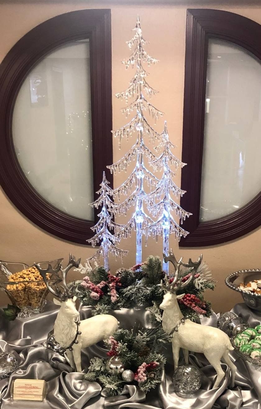 Silver Christmas tree centerpiece with reindeer figurines and holiday greenery on a table, in front of round mirrors