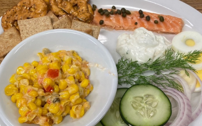 Assorted seafood platter with salmon, shrimp, salad, corn salad, bread, and sliced vegetables on a plate