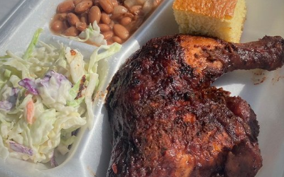 Takeout tray with fried chicken leg, coleslaw, baked beans, and cornbread