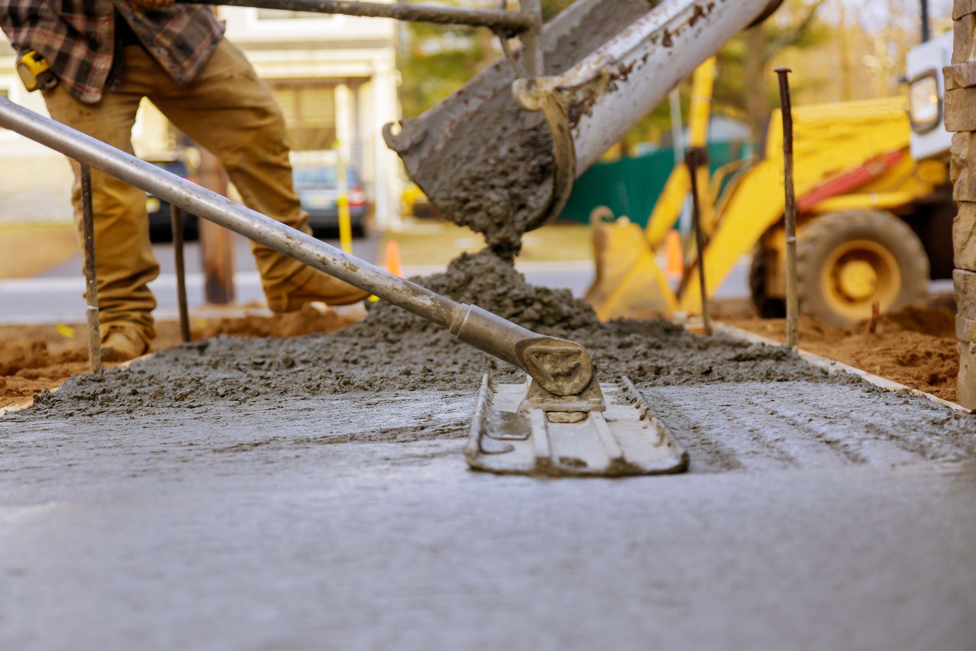 Construction worker leveling wet concrete with a bull float on a site with machinery in the background