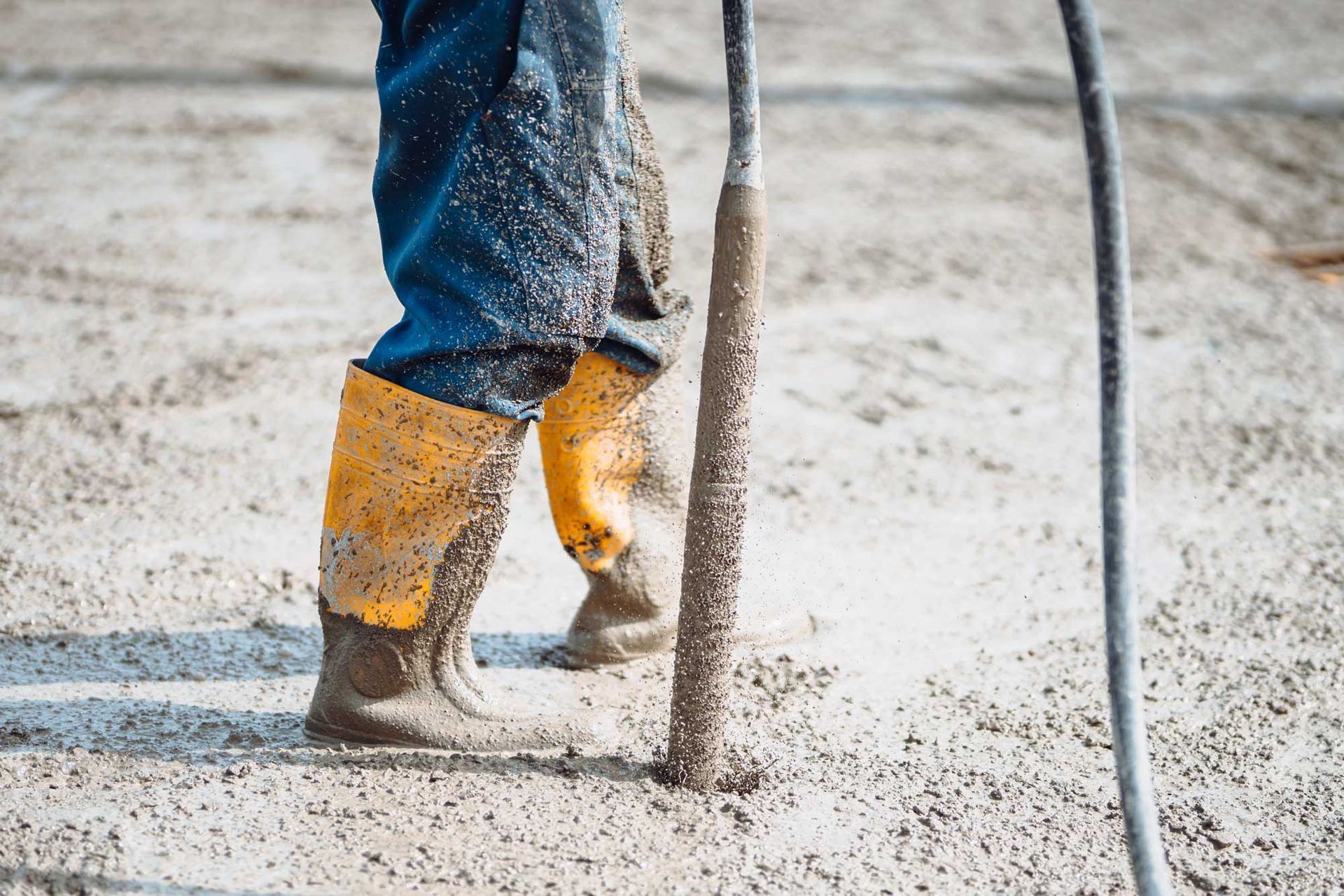 Worker in yellow boots standing in wet concrete, holding a tool at a construction site.