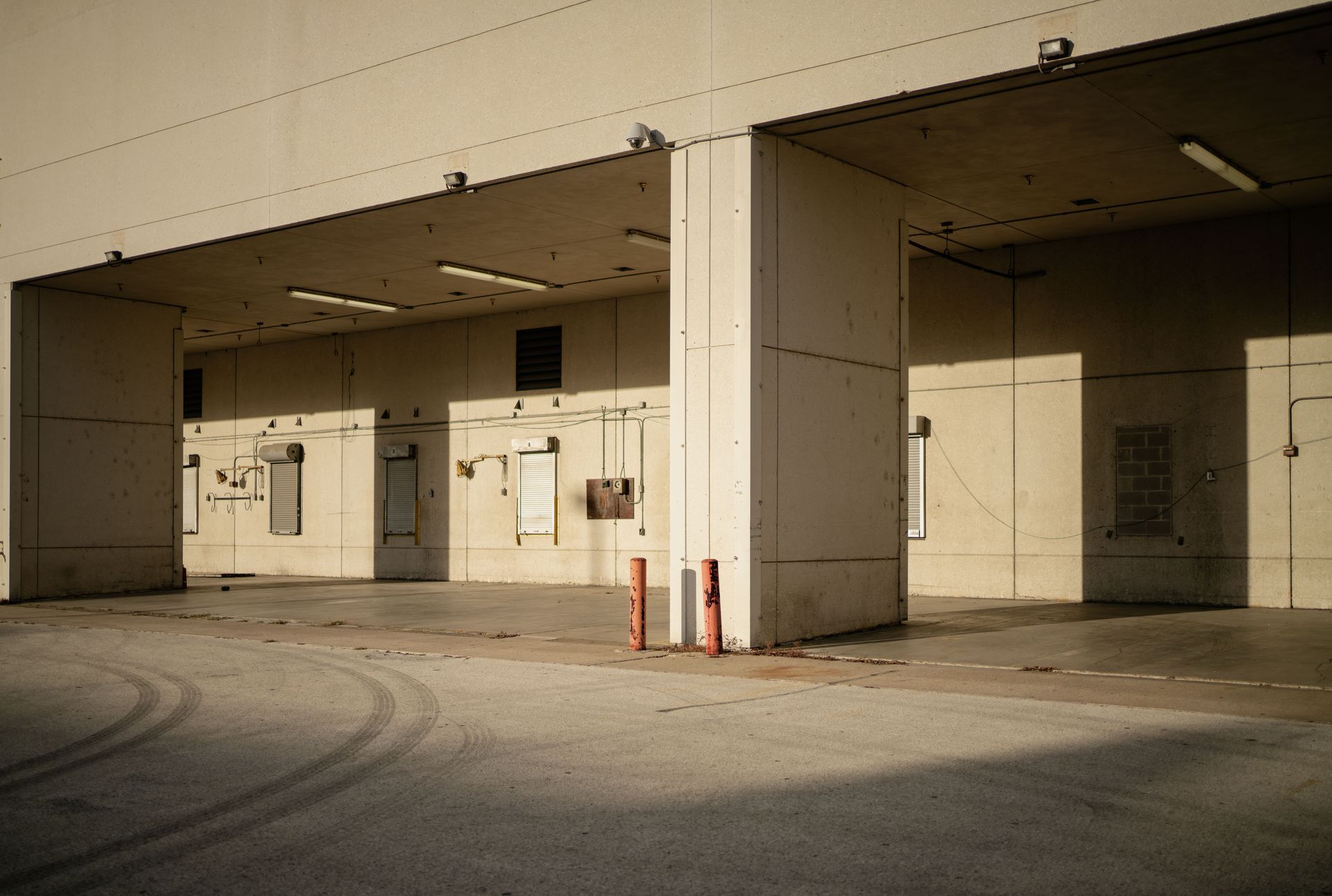 Empty industrial loading bay with beige concrete walls, red bollards, and sunlit pavement