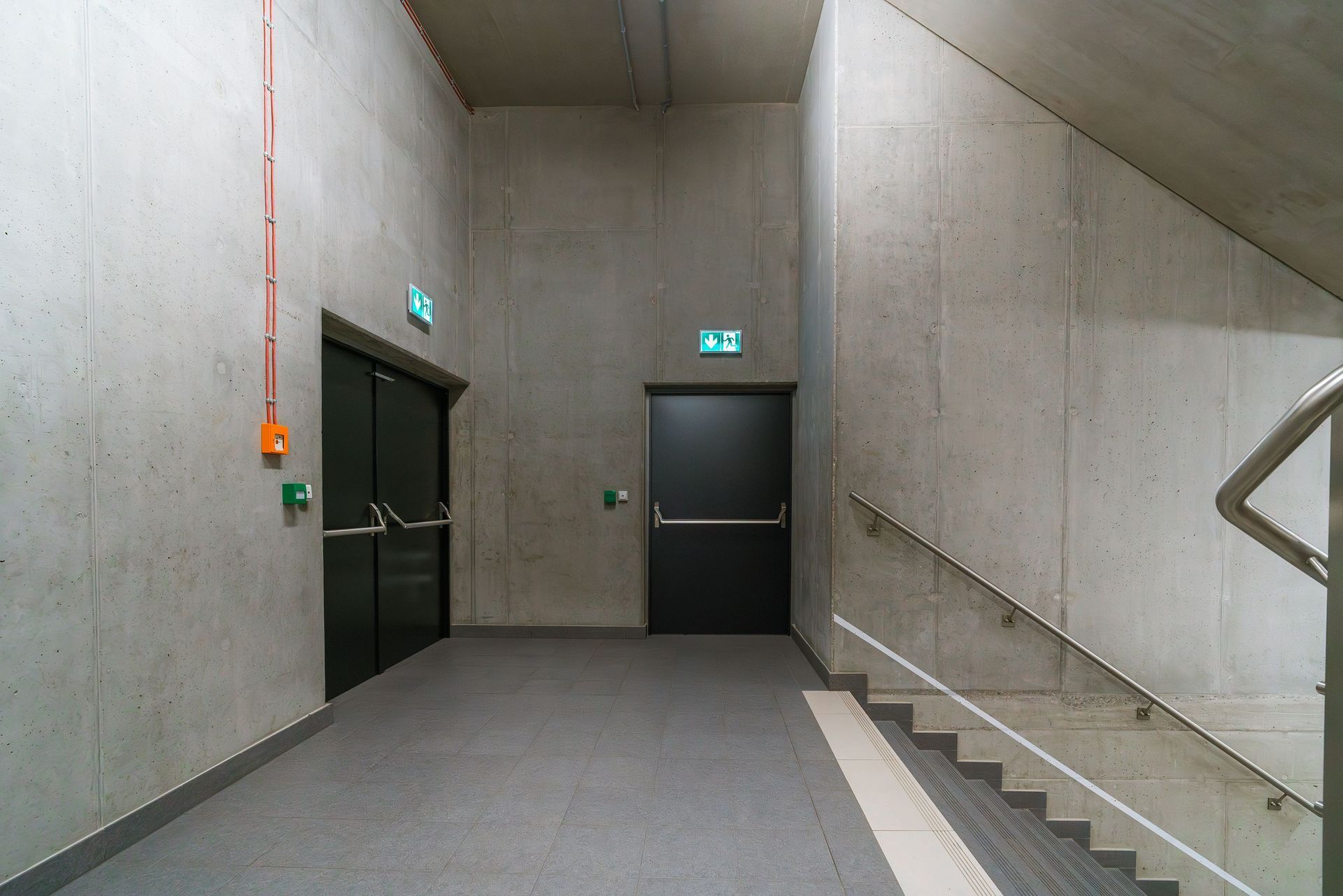Concrete hallway with two dark doors and stairway on the right.