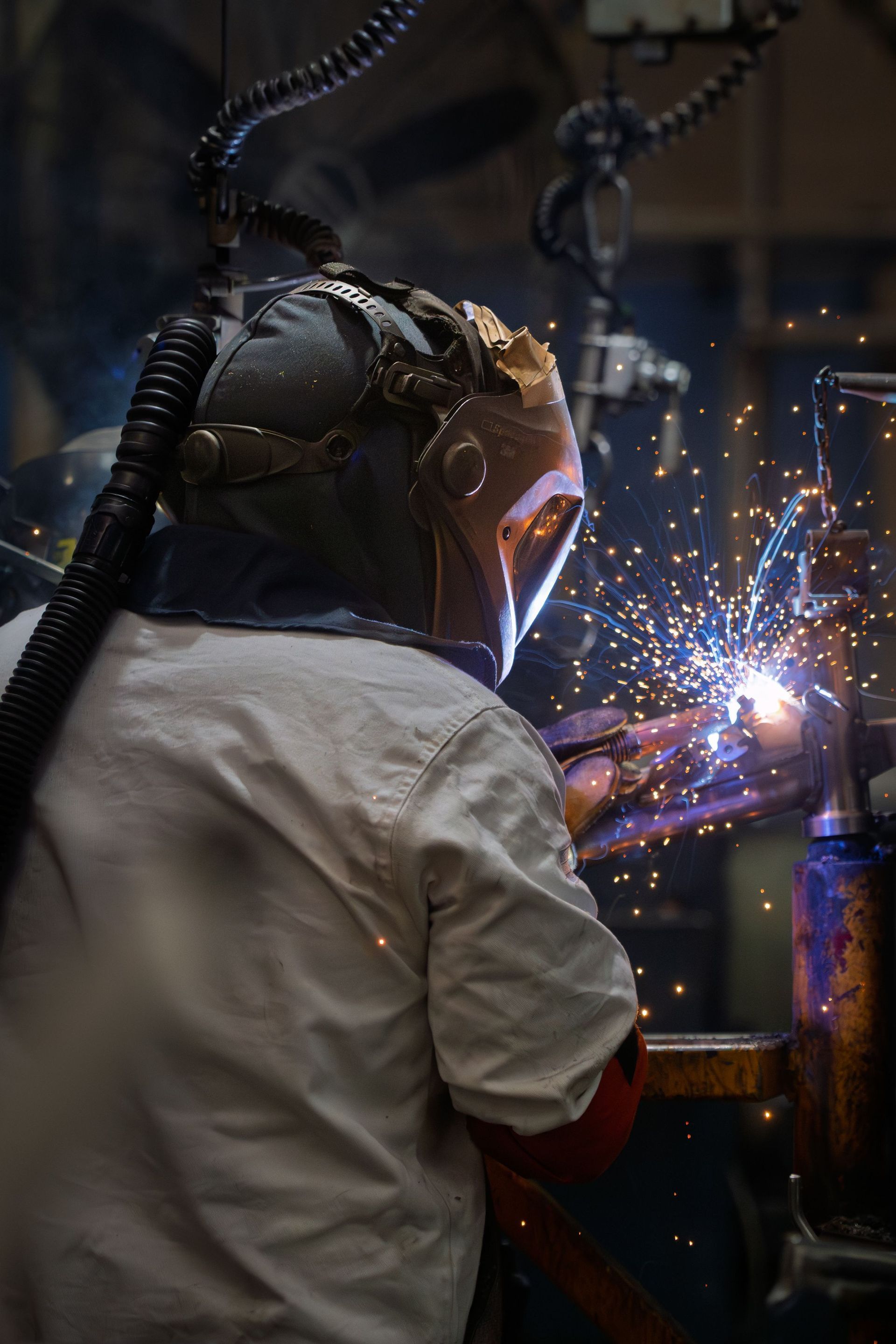 Welder in protective gear sparks metal in a dim workshop