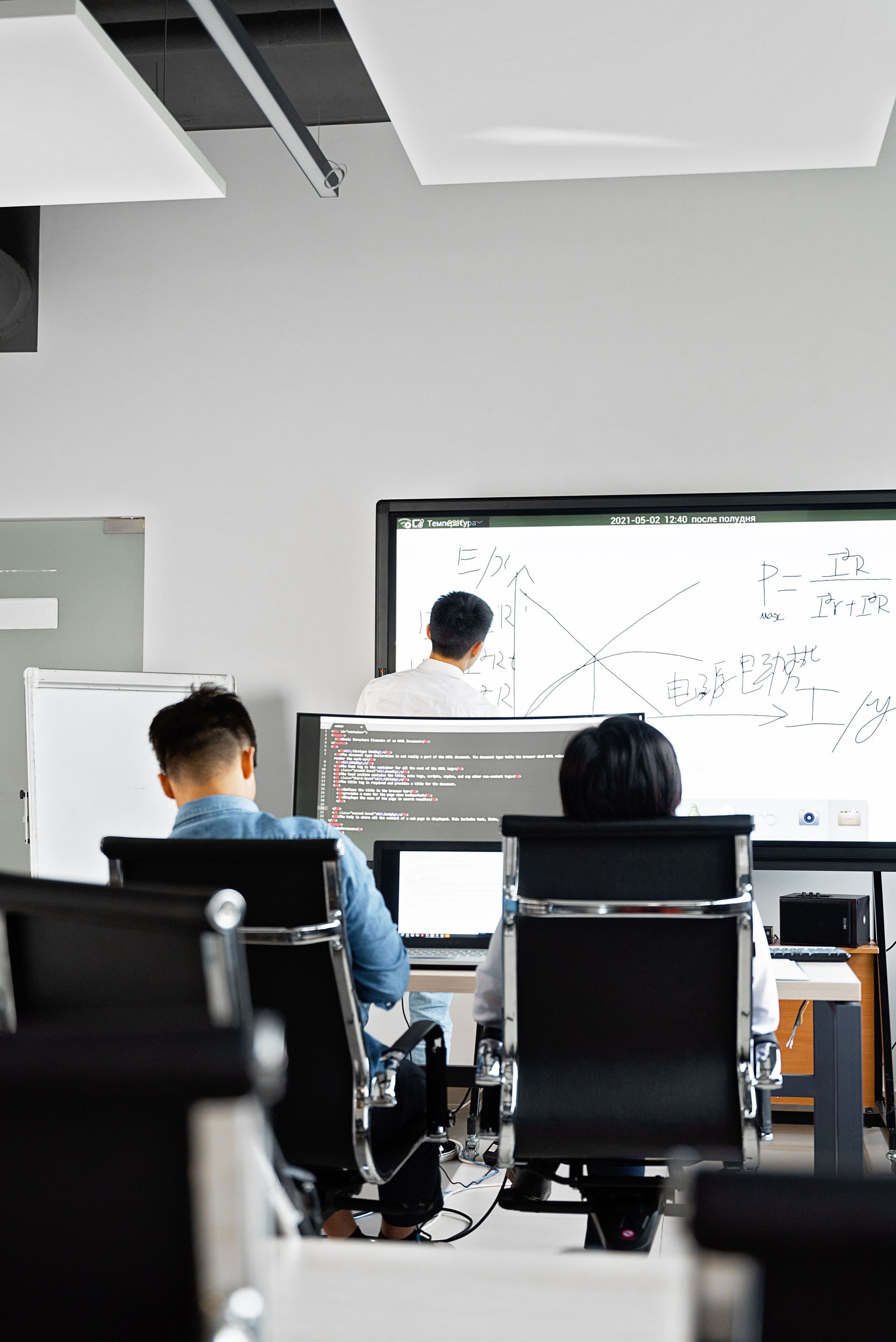 People seated in a classroom facing a presenter at a whiteboard.