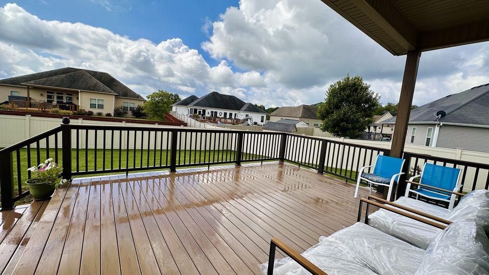 Wooden deck overlooking a green lawn and neighboring houses under a cloudy sky; two blue chairs and a white sofa with cushions are on the deck.