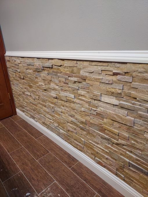 Stone accent wall with white baseboard and crown molding, next to a wood floor and door.