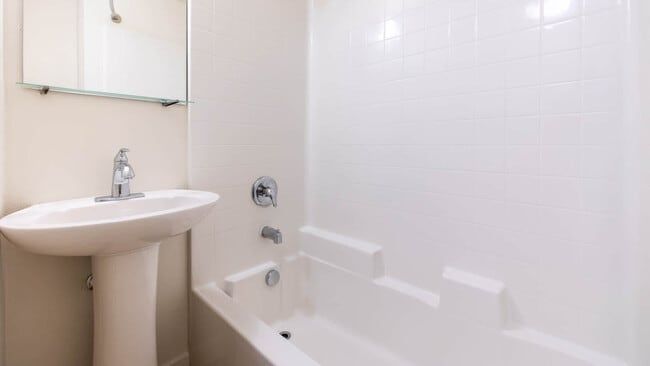 White bathroom with pedestal sink, tub/shower combo, and a mirror.