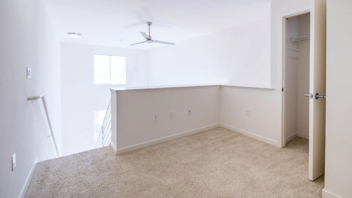 Empty loft bedroom with beige carpet, white walls, and open closet.