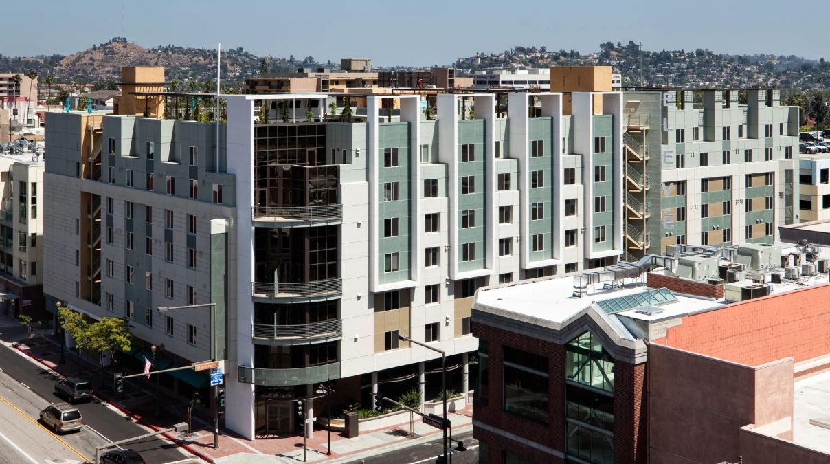Multi-story building with light green and beige facade; street level view with cars and sidewalks.