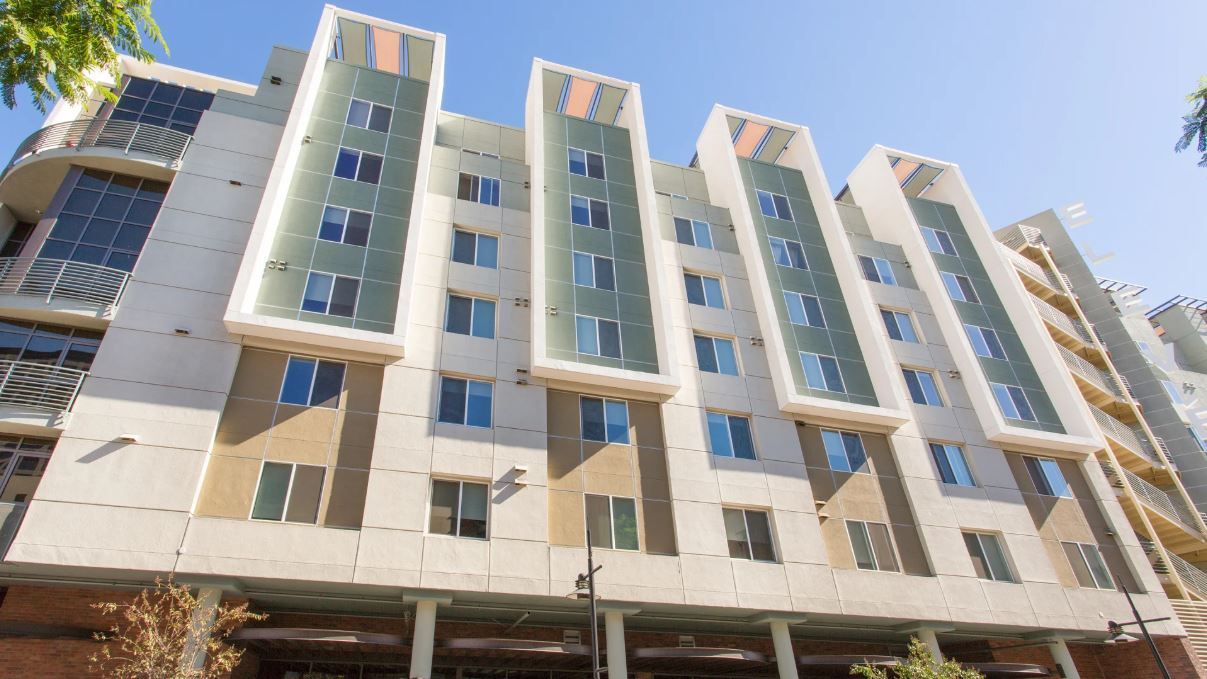 Modern multi-story apartment building with beige and green panels, blue sky.